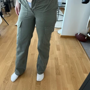 Olivgröna cargobyxor från Zara - Som ni ser får jag inte på mig dom och det är såklart anledningen till att jag säljer dom. Säljer ett par olivgröna cargobyxor från Zara med raka ben och flera praktiska fickor på sidorna. Byxorna har normal passform och stängs med dragkedja och knapp. Perfekta för en avslappnad stil. Det är storlek 34. Typ de skönaste och stilrenaste Cargo byxorna jag har haft på mig så de suger att dom är för små nu. Använts 1 gång. De ser grönare ut på bilden än vad de är. Bild nummer 3 beskriver bäst. 