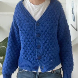 Blå stickad kofta från Monki - Säljer en blå stickad kofta från Monki med stora knappar framtill och bubblig struktur. Superfin till sommaren och bra kvalite. Den har inga defekter. Nypris: 399kr