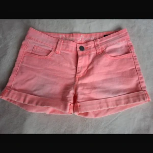 Rosa jeansshorts med uppvik - Snygga ljusrosa jeansshorts med klassisk femficksdesign och uppvikta benslut. Perfekta för varma dagar och har en knapp och dragkedja framtill. Passar dig som gillar en fräsch och färgglad stil.