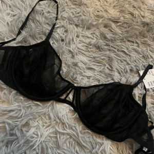 Svart mesh-bh från H&M - Säljer en svart bh från H&M i transparent mesh med tunna axelband och klassisk knäppning bak. Helt oanvänd och prislappen kvar, tyvärr inte originalförpackningen.