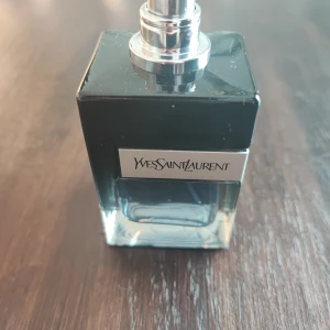 50 ml Parfym från Yves Saint Laurent - Elegant parfymflaska från Yves Saint Laurent med en stilren design. Flaskan är fyrkantig och har en mörk tonad glasfärg med en silverfärgad spraypump. Perfekt för den som söker en lyxig doftupplevelse.