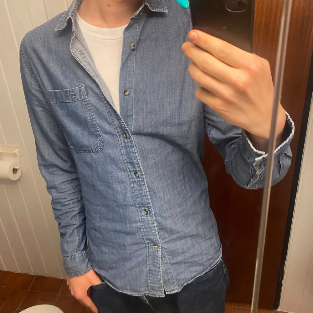 Säljer en snygg blå jeansskjorta med knappar framtill. Skjortan har en klassisk krage och en bröstficka. Perfekt för en avslappnad stil.. Paidat.