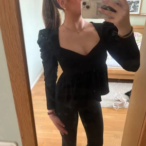 Svart långärmad topp från Gina Tricot - Säljer en svart långärmad topp från Gina Tricot med fyrkantig ringning och puffiga axlar. Toppen har en lätt volang nedanför bysten och är tillverkad i ett mjukt, stretchigt material. Perfekt för att lyfta din outfit!