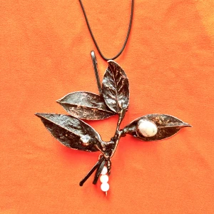 Halsband med blad och pärlor - Unikt halsband med ett stort metallblad som hänge, dekorerat med vita pärlor och svarta detaljer. Hängs i ett svart snöre och har en naturinspirerad design som sticker ut.