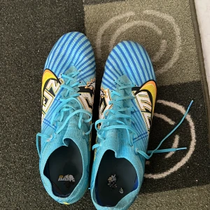 Blåa Nike fotbollsskor med grafiskt mönster - Säljer ett par blåa Nike fotbollsskor med snörning och grafiskt mönster i vitt, svart och gult. Sålde pga att de va för stora. Tar emot byte med fotbollsskor i storlek 46