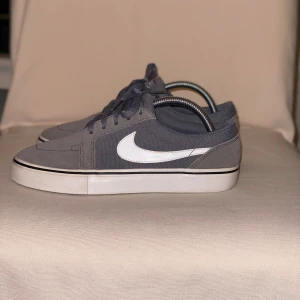 Grå sneakers från Nike - Snygga grå sneakers från Nike med mocka detaljer. Små ”fläckar” uppepå loggans sida (se bild), däremot inget man tänker på. Sko blocken ingår ej! 🥰