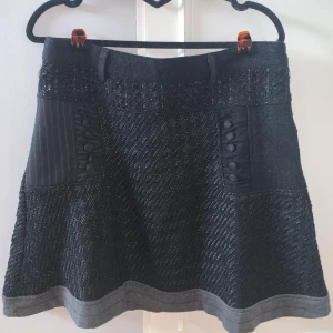 Svart kjol från Desigual - Snygg svart kjol från Desigual med unika texturer och detaljer. Kjolen har en mix av material och mönster som ger en cool look. Perfekt för att sticka ut med stil!