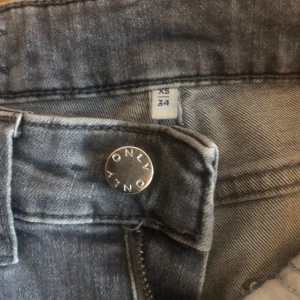 Grå bootcut jeans från ONLY, XS/34 - Snygga grå jeans från ONLY i bootcut-modell. Klassisk femficksdesign, normalhög midja och dragkedja med knapp framtill. Jeansen är i mjukt denimtyg och passar perfekt till en avslappnad stil. De har lite fransig kant nertill på bakre vänsterbenet annars i mycket gott skick!