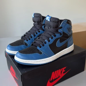 Nike Air Jordan 1 Retro High OG Marine Blue - Nike Air Jordan 1 Retro High OG i mörkblått och svart skinn med vita detaljer. Klassisk high-top siluett med svart swoosh, perforerad tå och svart snörning. Kommer med extra vita skosnören och originalkartong. Perfekta för dig som gillar streetstyle. Kommer med Crease Protecters och 2 extra snören 😁
