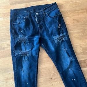 Mörkblå Dsquared2 skinny jeans med slitningar - Snygga mörkblå skinny jeans från Dsquared2 med slitna detaljer, patchar och färgstänk på benen. Klassisk femficksmodell med silverfärgade nitar och dragkedja. Jeansens material är bomull med stretch för skön passform.