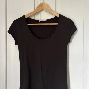 Svart kortärmad topp från Zara - En mörk brun enkel och stilren topp från Zara TRF i ekologisk bomull. Modellen har korta ärmar, rundad djup ringning och en figurnära passform. Perfekt att matcha med jeans eller kjol för en clean look. Mjuk och skön mot huden. Obs! Hund och katt finns i hemmet samt så tvättas plagget innan jag skickar iväg det!