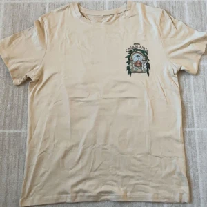 Beige Casablanca t-shirt med tryck - Sprillans ny nygg beige t-shirt från Casablanca med coolt grafiskt tryck på både bröstet och ryggen. Har inte ens haft på mig den och säljer den då jag har bytt stil. Säljer den för billigt redan men priset kan diskuteras👍👌