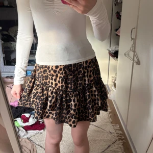Leopardmönstrad volangkjol - Supersöt kort kjol med leopardmönster och volanger. Kjolen har en brun och svart färgskala och sitter snyggt i midjan. Perfekt för dig som vill sticka ut lite extra med en trendig look.