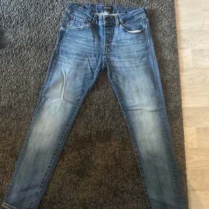 Blå skinny jeans Jack & Jones 30/30 - Säljer ett par blå skinny jeans från Jack & Jones med superstretch. Jeansen har klassisk femficksdesign, snygga slitningar och smal passform. Perfekta för dig som gillar en tajt look och vill ha bekväma jeans som sitter snyggt hela dagen.