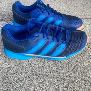 Adidas inneskor  - Snygga blå Adidas sneakers med coola detaljer och klassiska ränder på sidorna. Skorna har snörning, slitstark gummisula i beige och blått samt ventilerande meshpartier. Perfekta för dig som gillar sport. Köpta för innebandy men korsbandet drogs…