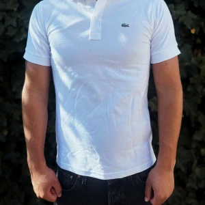 Vit Lacoste pikétröja i bomull - Fräsch vit pikétröja från Lacoste med klassisk krage och korta ärmar. Tröjan har den ikoniska gröna krokodilloggan broderad på bröstet och knäppning med två vita knappar. Tillverkad i mjuk bomull som andas, perfekt för en clean och stilren look.                                                                                                                                                                               Nypris: 1350kr GORILLAPRIZE:755kr     Skick:10/10 oöppnad      KVITTO MEDKOMMER