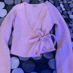Ljusrosa omlottkofta från Gina Tricot - Superfin ljusrosa omlottkofta från Gina Tricot med knyt i sidan och v-ringad hals. Koftan är stickad, har långa ärmar och en croppad passform som ger en trendig look. Perfekt att slänga på sig över ett linne eller t-shirt. den är i bra skick , använd 2 gånger. inga fläckar eller hål på tröjan ❣️den är i storlek M, jag säljer den då jag inte kan använda storlek M 💞