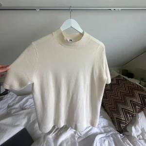 Vit kashmir polotopp från Uniqlo - En stilren vit stickad kashmir  polotopp från Uniqlo med korta ärmar och ribbad hög krage. Enkel och clean design som passar perfekt till jeans eller kjol. Mjuk och skön kvalitet som känns lyxig mot huden.