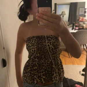 Leopardmönstrad bandeau tubtopp - Säljer en leopardmönstrad bandeau tubtopp med volangig nederdel. Toppen är axelbandslös och har en smockad midja som ger en snygg passform. Perfekt för dig som vill sticka ut med ett djurmönster och en cool vibe.