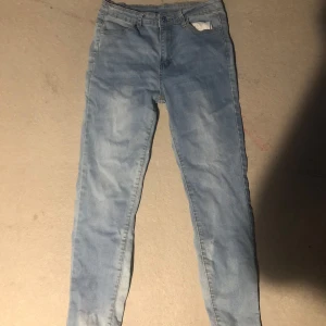 Ljusblå skinny jeans med stretch - Säljer ett par ljusblå skinny jeans med klassisk femficksdesign och snyggt slitna detaljer. Jeansen har normal midja, smal passform och är tillverkade i stretchigt denim för extra komfort. Perfekta till sneakers eller boots.