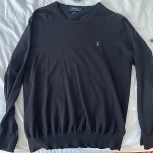 Svart tröja från Polo Ralph Lauren - Snygg svart tröja från Polo Ralph Lauren med rund hals och diskret logga broderad på bröstet. Tröjan har långa ärmar och ribbade muddar vid ärmslut och nederkant. Perfekt för dig som gillar klassisk och stilren design.