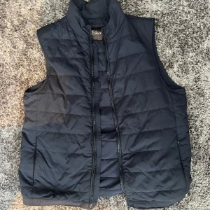 Mörkblå  dunväst från Oscar Jacobson - Stilren mörkblå dunväst från Oscar Jacobson. Väldigt bra skick förutom att ugglan är sönder.