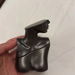 Eilish No. 2 parfym Billie Eilish - Unik parfymflaska formad som en byst i mörkgrå metall-look från Billie Eilish, modell Eilish No. 2. Flaskan har en modern och edgy design med mattsvart finish och stilren signatur på baksidan. Perfekt för dig som gillar coola detaljer på sminkbordet.