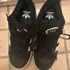 Svarta Adidas Campus sneakers i mocka - Klassiska med vita ränder och logga på hälen. Skorna har snörning, vit sula och gummiyttersula. Perfekta för en streetstyle-look och funkar året runt. Jag köpte dem i maj men inte använt de så mycket pga fel storlek. De är inte smutsiga i tyget men på sulan, se bild. Storlek 37 1/3