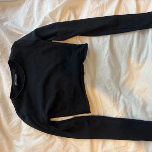 Svart croppad långärmad topp - En svart, croppad långärmad topp från Bik Bok. Enkel och stilren design med rund halsringning och tight passform. Perfekt att matcha med höga jeans eller shorts för en clean look.