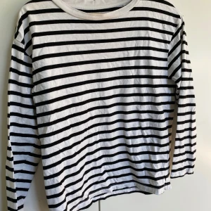 Randig långärmad tröja från 157 - Säljer en vit och svart långärmad tröja från 157 i storlek XS. Tröjan har klassiska horisontella ränder och är gjord i mjuk 100% bomull. Perfekt för dig som gillar enkel och stilren design med lite fransk vibe.