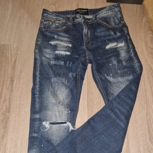 Mörkblå slitna jeans från Supply & Demand - Säljer ett par mörkblå jeans i storlek 30 i midja, från Supply & Demand med snygga slitningar. Jeansen är i en lite smalare form. Använts som högst 5 gånger, dunder kvalitet!