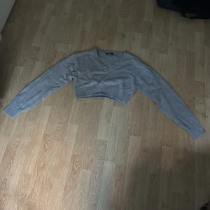Grå croppad stickad tröja Gina Tricot - Säljer en grå croppad stickad tröja från Gina Tricot i storlek L. Tröjan har v-ringad hals, långa ärmar och bred ribbad kant nedtill. Perfekt för dig som gillar en loose och chill stil. Superenkel att matcha med jeans eller kjol.