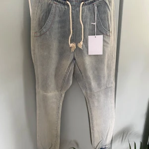Ivory Super Trackie från OneTeaspoon - Snygga ivoryfärgade trackpants från OneTeaspoon i denim. Byxorna har resår och snörning i midjan, avslappnad passform och cool tvättad look. Perfekta för en chill och trendig stil. Materialet är jeans och de har synliga kontrastsömmar.
