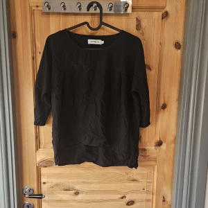 Svart blus från Size Needle - En enkel svart blus från Size Needle med rund halsringning och trekvartsärm. Tillverkad i ett lätt och luftigt tyg som passar perfekt till både jeans och kjol. Stilren och tidlös modell som är lätt att matcha.