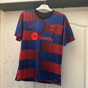 FC Barcelona Nike matchtröja blå/röd - Säljer en FC Barcelona matchtröja från Nike med Spotify-logga. Tröjan har korta ärmar och är tillverkad i ett lätt, ventilerande material. Framsidan har ett randigt mönster i blått och rött med klubbmärke och Nike-logga. Baksidan är mestadels svart.