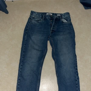 Blå raka jeans från fsbn 30W/32L - Säljer ett par klassiska blå jeans från fsbn med raka ben och normal passform. Jeansen har knäppning med knappar framtill, fem fickor och snyggt tvättad denim. Perfekta för en avslappnad stil och funkar året runt.