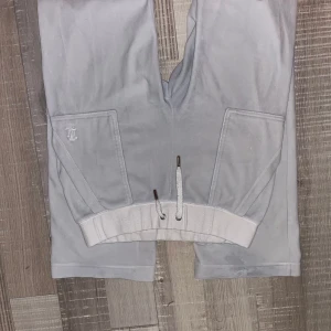 Ljusgrå mjukisbyxor Juicy Couture S - Säljer ett par ljusgrå mjukisbyxor från Juicy Couture med bred resår och snörning i midjan. Byxorna har stora fickor fram, en ficka med knappar på benet och broderad JC-logga. Perfekta för chill dagar eller när du vill vara extra comfy.