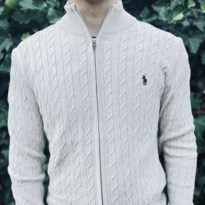 Vit kabelstickad kofta från Ralph Lauren - Snygg beige kabelstickad kofta från Ralph Lauren med dragkedja framtill och klassisk broderad logga på bröstet. Tröjan har hög krage och lång ärm, perfekt för lager-på-lager. Mjuk och skön känsla i bomullsmaterial..     Nypris: 3145kr GORILLAPRIZE:1680kr             Skick:10/10 oöppnad          KVITTO MEDKOMMER 