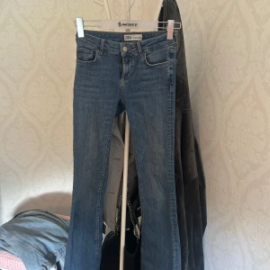 Blå bootcut jeans från Zara, stl 34 - Snygga blå jeans från Zara i storlek 34. Modellen har bootcut-ben och klassisk femficksdesign. Jeansen är tillverkade i mjukt denimtyg och har normal passform med medelhög midja. 