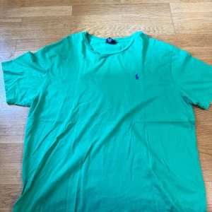 Grön t-shirt från Ralph Lauren - Fräsch grön t-shirt från Ralph Lauren med klassisk lila broderad logga på bröstet. T-shirten har rund halsringning och korta ärmar. Perfekt basic-plagg med snygg färg och skön bomullskänsla.