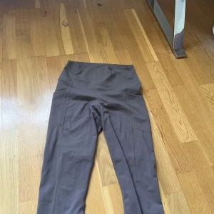 Bruna leggings från Athletika Couture - Snygga bruna leggings från Athletika Couture i stretchigt material med hög midja och praktiska sidfickor. Perfekta för träning eller chill, tillverkade i polyester och spandex för maximal komfort och rörelsefrihet.