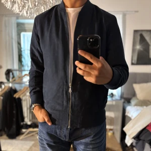 Mörkblå bomberjacka från Jack & Jones - Snygg mörkblå bomberjacka från Jack & Jones med klassisk passform. Jackan har dragkedja framtill, ribbade muddar och två sidofickor. Tillverkad i mjuk bomullsmix som känns skön mot kroppen. Perfekt för dig som vill ha en stilren och enkel look.