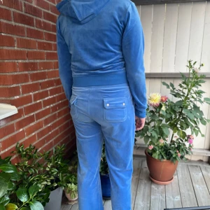 Blått Juicy Couture Sett - Säljer ett blått juicy couture sett i mjuk velour med raka ben och bred resår i midjan. Byxorna har fickor fram och bak. Nypris: 2500kr