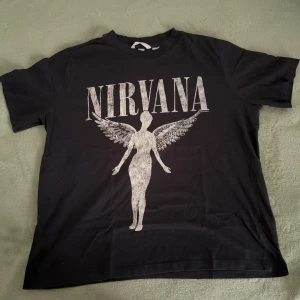 Svart Nirvana t-shirt  - Säljer en svart oversized t-shirt från H&M med stort Nirvana-tryck. Perfekt för dig som gillar bandmerch och vill ha en cool, avslappnad stil.