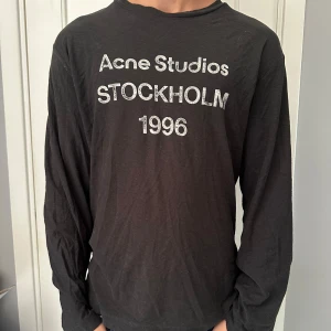 Svart långärmad tröja Acne Studios - Svart långärmad tröja från Acne Studios med vit text 'Acne Studios STOCKHOLM 1996' på bröstet. Tröjan har en avslappnad passform och är tillverkad i mjuk bomull, perfekt för en stilren och enkel look. Nypris 3500kr! Mitt pris 2000