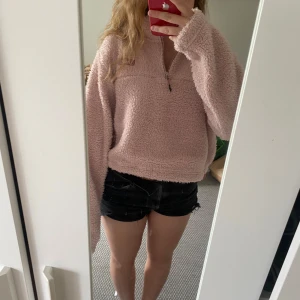 Rosa fleece half zip från Nike - Supermjuk och fluffig rosa fleece från Nike med halv dragkedja och liten logga på bröstet. Croppad modell med lång ärm och relaxed fit, perfekt för kyliga dagar. Fickdetalj med dragkedja på sidan. Så mysig och trendig att slänga på sig!