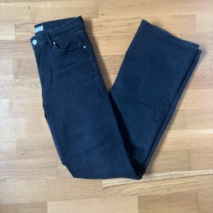 Svarta bootcut jeans från Lindex - Snygga svarttvättade jeans från Lindex med bootcut-modell och klassisk femficksdesign. Jeansen har hög midja och är tillverkade i ett stretchigt bomullsmaterial som sitter skönt och formar sig efter kroppen. Perfekta för dig som gillar en tidlös och clean look.