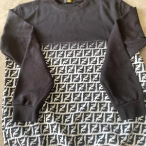 Fendi tröja - Cool svart sweatshirt med lång ärm och rund hals. Nedre delen har ett grafiskt svartvitt mönster som ger en unik vibe. Överdelen och ärmarna är helsvarta. Perfekt för dig som gillar streetstyle och vill sticka ut lite extra.
