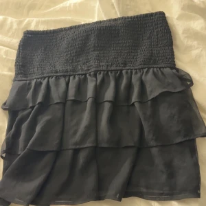 Svart volangkjol med smock - Om du är intresserad skriv innan du köper!   Supersöt svart kortkjol med bred smock i midjan och flera lager volanger. Kjolen har en flowy känsla och passar perfekt till en cool topp eller hoodie. Enkel att styla och riktigt skön att bära.