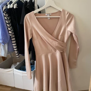 Beige omlottklänning från NLY One - Supersnygg beige kortklänning från NLY One med omlott och v-ringning. Klänningen har långa ärmar och en lätt utsvängd kjol som ger en feminin siluett. Perfekt för dig som gillar stilrena och enkla plagg med en twist.